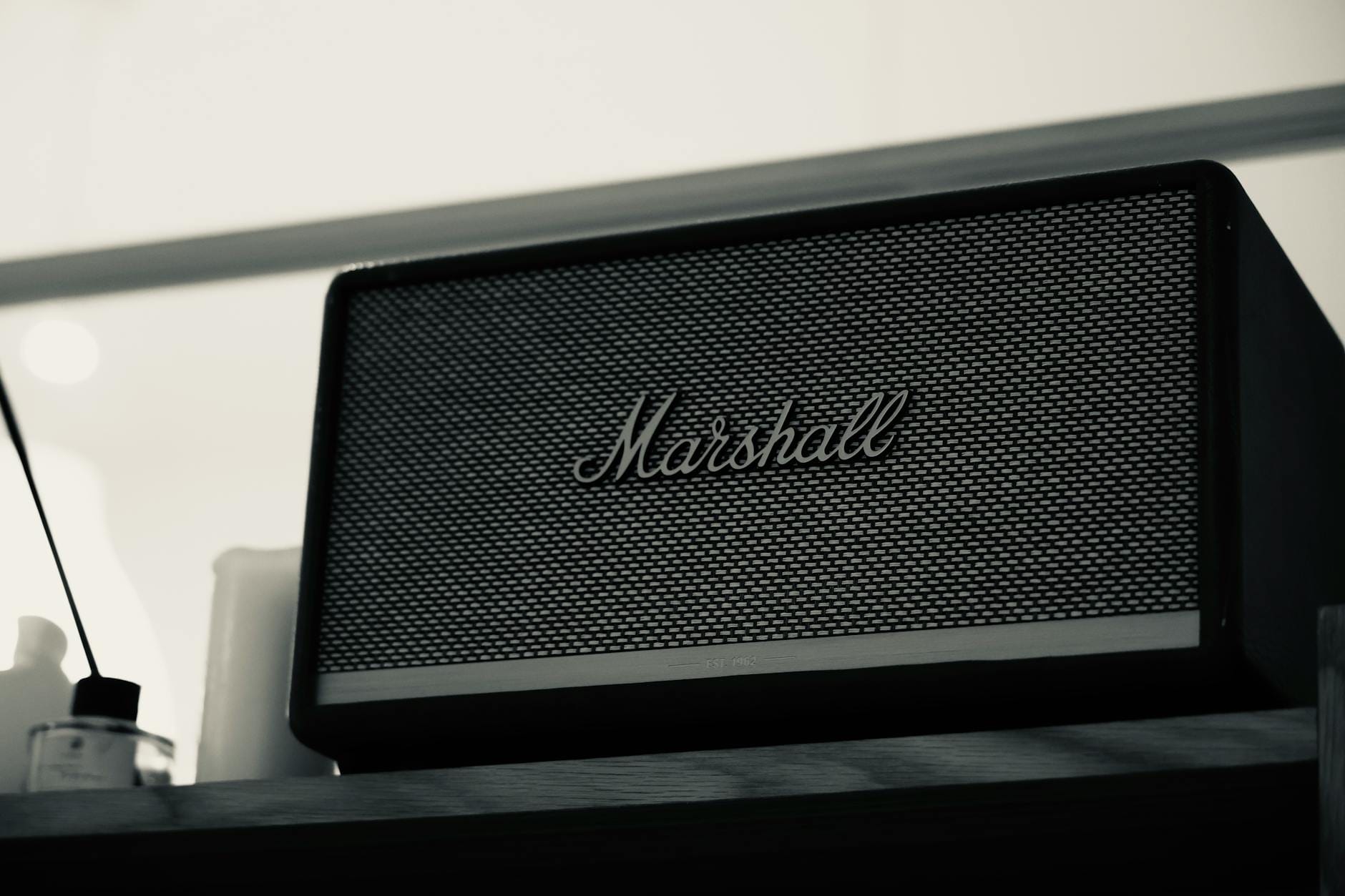 Czarny głośnik Marshall Bluetooth na drewnianej półce w pokoju