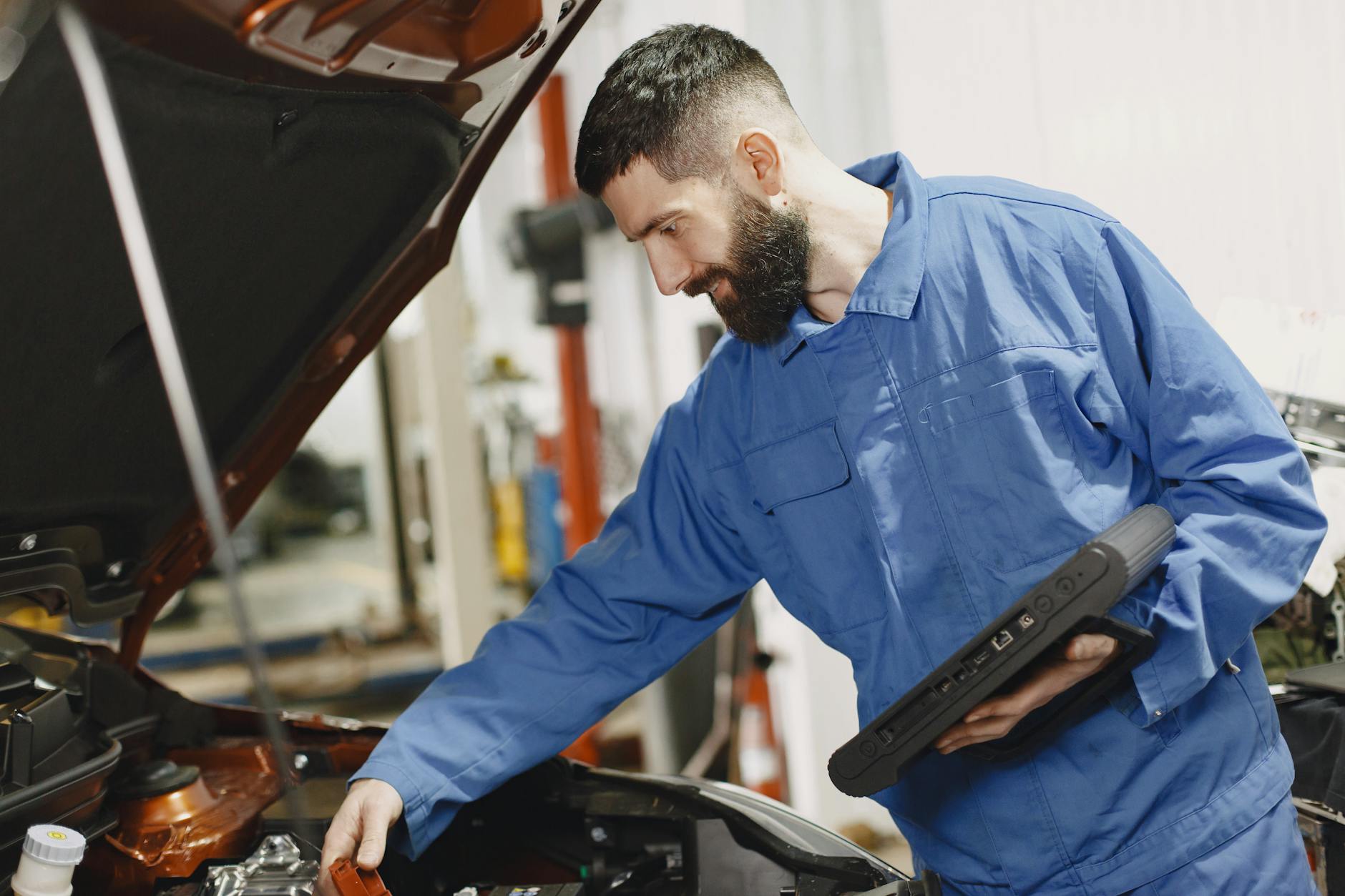 Mechanik samochodowy w niebieskim kombinezonie sprawdza silnik w garażu