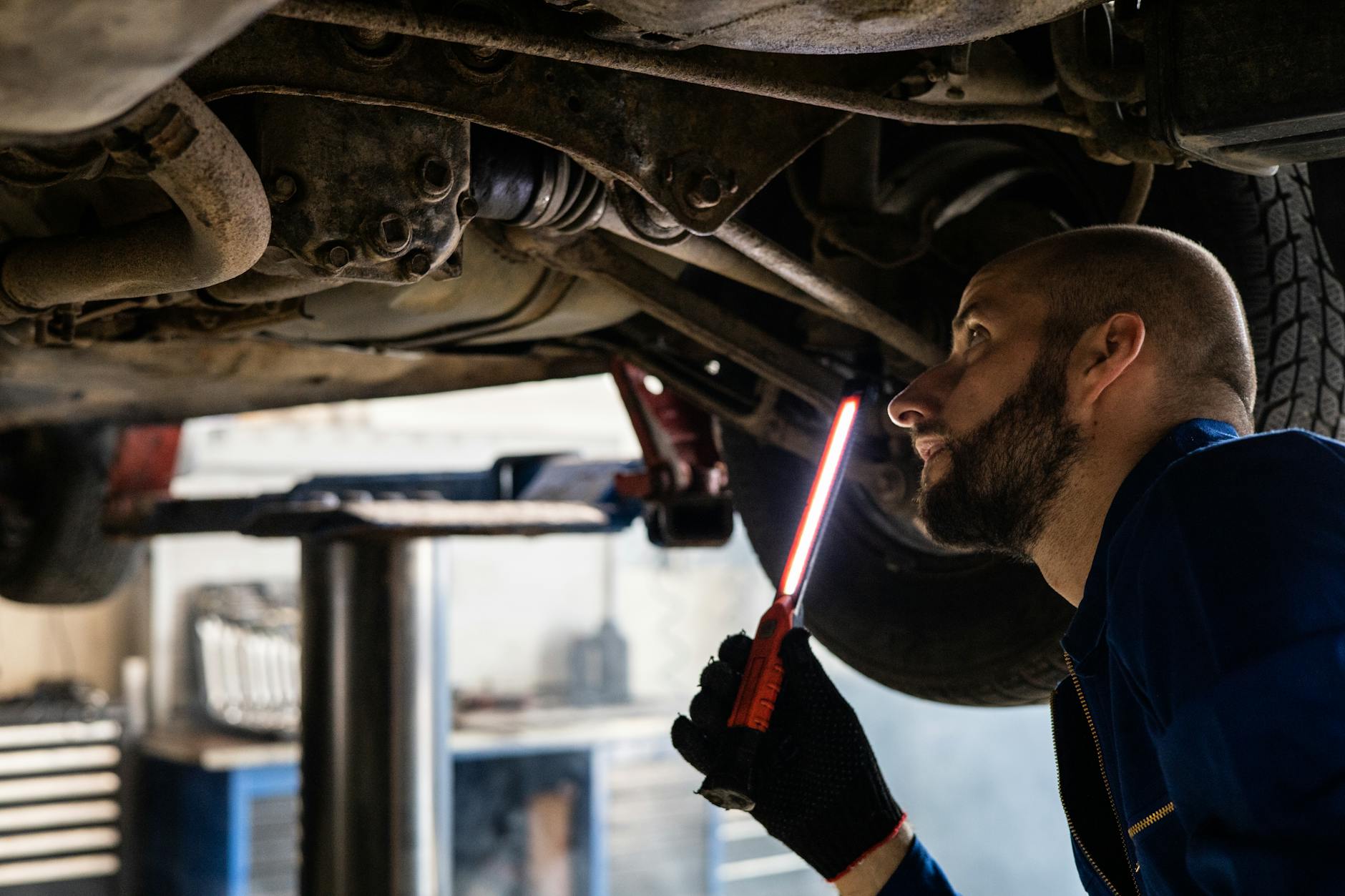 Mechanik z latarką diagnozuje podwozie samochodu w warsztacie