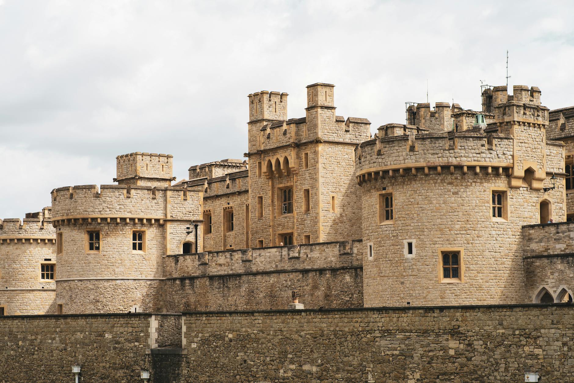 Zewnętrzna fasada Tower of London z kamiennymi murami pod chmurnym niebem